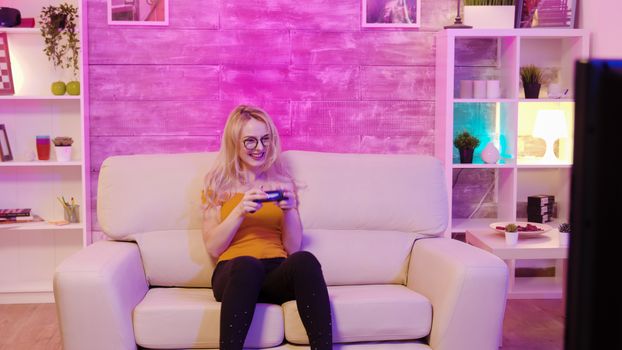 Beautiful blonde girl excited while playing video games using wireless controllers. Cheerful girl playing video games.