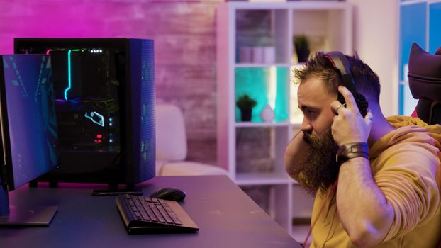 Concentrated man playing video games on pc in his room with colorful neons. Man playing video games during night.