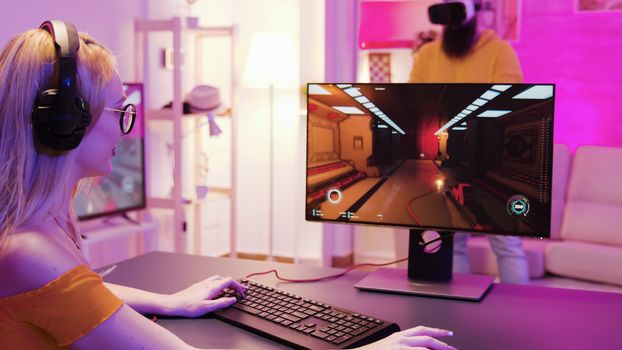 Girl playing shooter games in a room with colorful neon lights. Man with virtual reality headset.