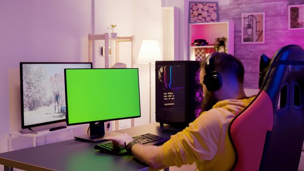 Man in his room relaxing playing video games on computer with green screen. Man sitting on gaming chair.