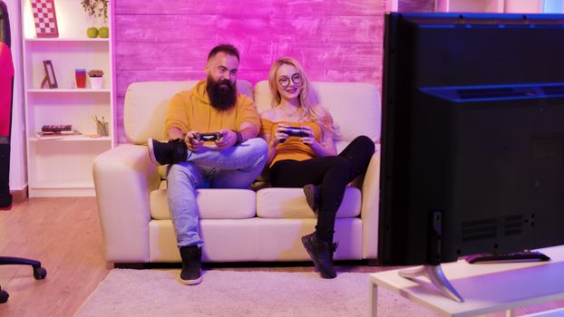 Revealing footage of beautiful young couple playing together video games on a big screen TV using wireless controllers.