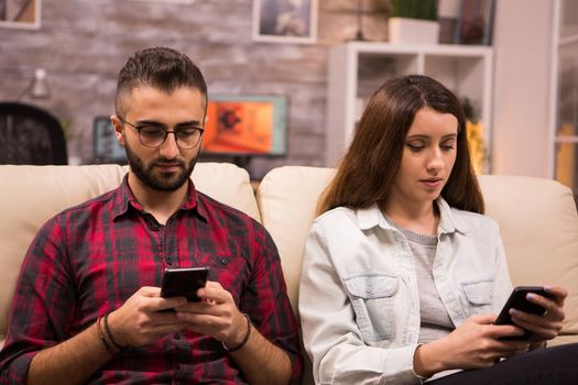 Young couple obsessed with smartphones checking social networks at sitting on couch.