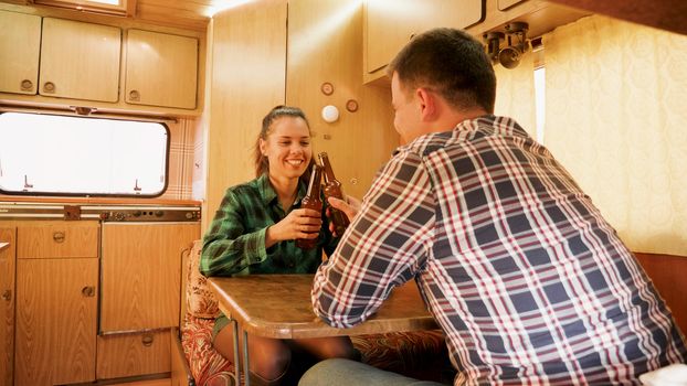 Husbnand making his wife laugh while she's holding a bottle of beer inside of their retro camper van.