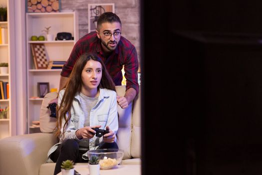 Boyfriend helping his girlfriend to play video games on television using controllers.
