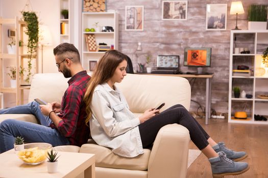 Upset couple sitting back to back on sofa in living room after a disagreement.