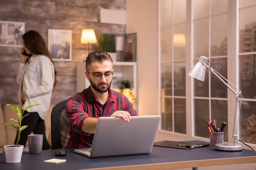 Caucasian young man opens laptop for work in living room.Girlfriend in the background.