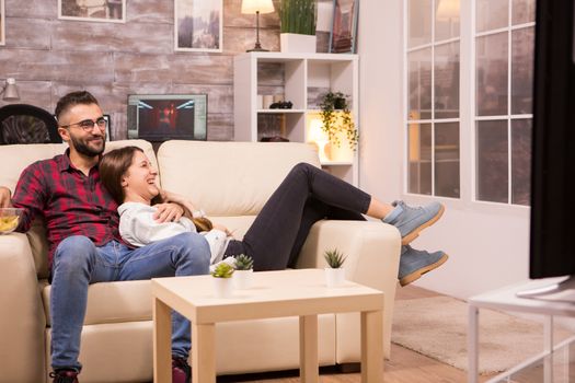 Couple laughing while watching a movie on tv and sitting on couch. Cheerful couple.