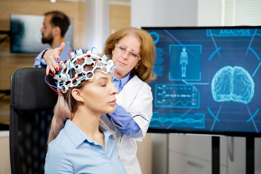 Doctor arranging neurology scanning headset for tests on a female patient. Scanning machine