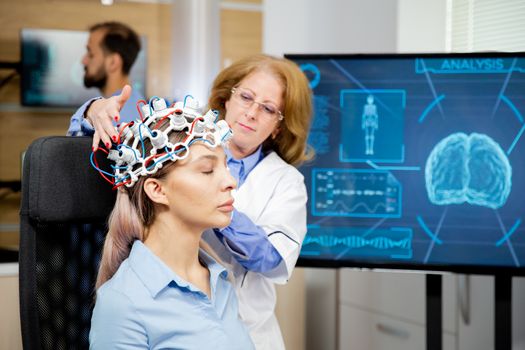 Doctor arranging neurology scanning headset for tests on a female patient. Scanning machine