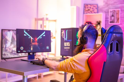 Bearded man playing online video games on his pc and talking with others players. Colorful neons in the room.