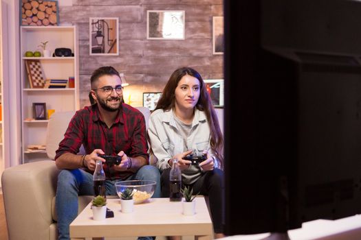 Relaxed couple playing video games on television using controllers. Couple sitting on couch.
