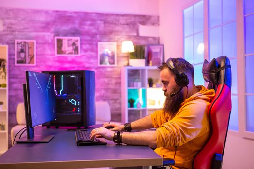Hipster man playing professional video games in his room with colorful neons. Man wearing headphones while playing video games.