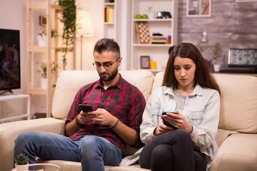 Boyfriend and girlfriend using their phones while sitting together on couch.