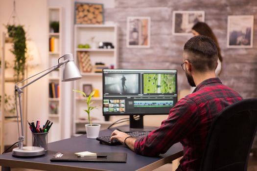 Back view of creative filmmaker working on a movie on laptop. Girlfriend in the background.