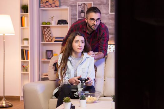 Boyfriend helping his girlfriend to win at video games. Girl playing video games on television using controllers.