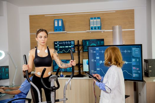 Fit female doing endurance test in the lab. Doctor makes notes in the tablet