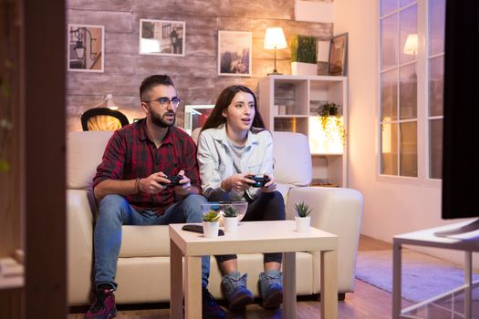 Young couple having a good time while playing video games on television. Couple sitting on sofa.
