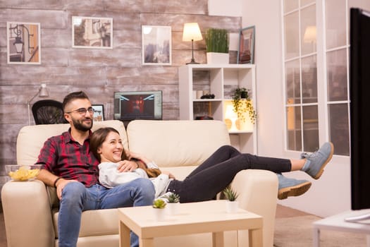 Beautiful young couple relaxing on sofa while watching a movie on tv.
