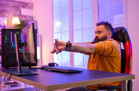 Bearded man sitting on gaming chair preparing to play online video games on pc. Room with colorful neons.