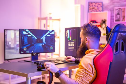 Bearded man playing online video games on his pc and talking with others players. Colorful neons in the room.