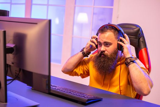 Hipster man playing professional video games in his room with colorful neons. Man wearing headphones while playing video games.