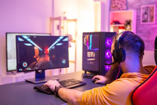 Hipster man playing professional video games in his room with colorful neons. Man wearing headphones while playing video games.