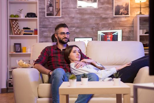 Beautiful young couple watching their favorite tv show while relaxing on couch at night.