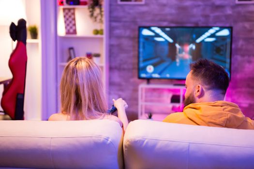 Young couple playing together online shooter games with wireless controllers. Couple playing videogames.