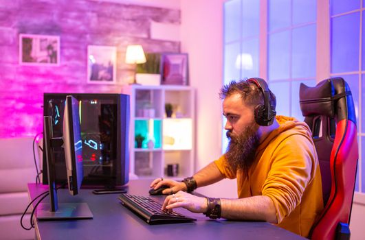 Concentrated bearded gamer looking at PC display in room with neon colors