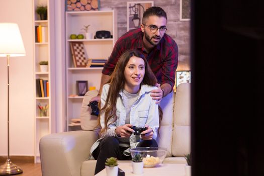 Boyfriend helping his girlfriend to win at video games. Girl playing video games on television using controllers.