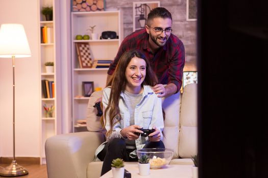 Happy young couple playing video games on television using controllers at night.