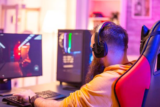 Hipster man playing professional video games in his room with colorful neons. Man wearing headphones while playing video games.