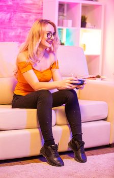 Beautiful blonde girl excited while playing video games using wireless controllers. Cheerful girl playing video games.