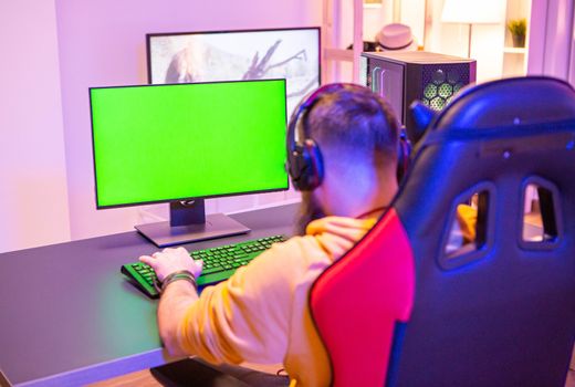 Man playing on powerfull gaming pc in a room with neon lights on a green screen computer.