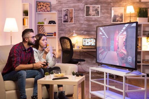 Man sitting on couch and playing video games on television while his girlfriend is eating chips.