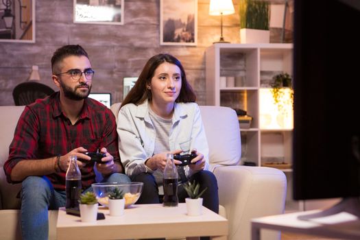 Cheerful couple playing video games at night using controllers. Couple sitting on couple.