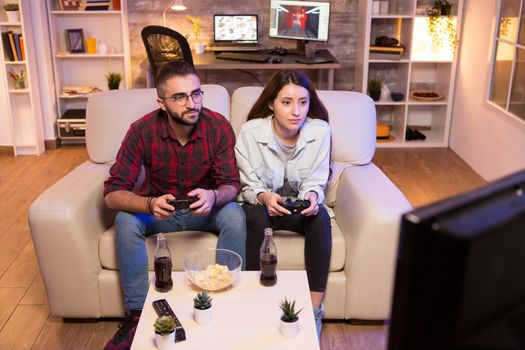 Concentrated young couple while playing video games on television. Couple sitting on couch.