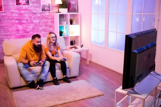 Beautiful young couple playing together online video games at home. Room with colorful neon lights.