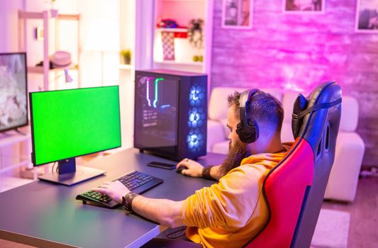 Man playing on powerfull gaming pc in a room with neon lights on a green screen computer.