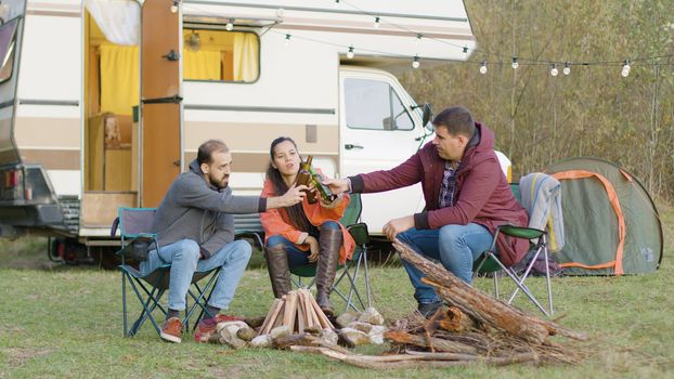 Carefree friends making a toast with beer before making camp fire. Retro camper van.