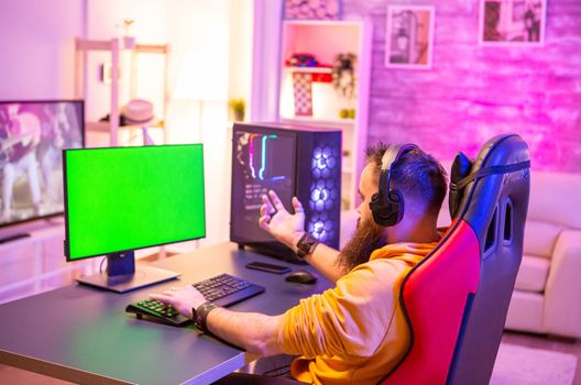 Man playing on powerfull gaming pc in a room with neon lights on a green screen computer.