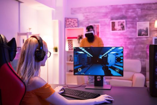 Boyfriend playing games using vr goggles while girlfriend having fun playing shooter games. Gaming chair.