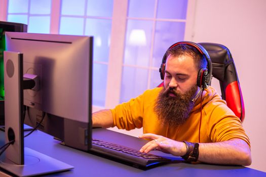 Hipster man playing professional video games in his room with colorful neons. Man wearing headphones while playing video games.