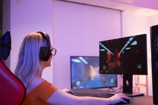 Side view of focused girl playing shooter games on her computer. Girl sitting on gaming chair.