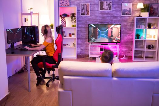 Blond girl playing shooters games in a room with neon light. Gamer girl on gaming chair.