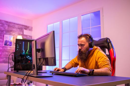 Professional gamer with long beard in front of powerful gaming rig in room full of neon lights