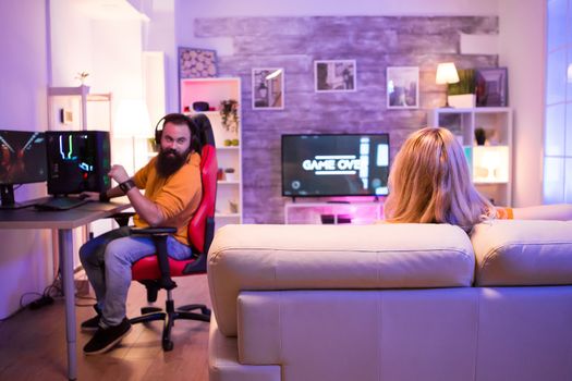 Back view of blond girl sitting on sofa in a room with colorful neon light. Game over for gamer girl.