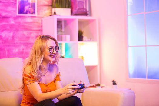 Beautiful blonde girl excited while playing video games using wireless controllers. Cheerful girl playing video games.