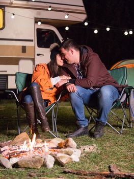 Beautiful young couple warming together near camp fire in a cold night of autumn in the mountains. Retro camper van.