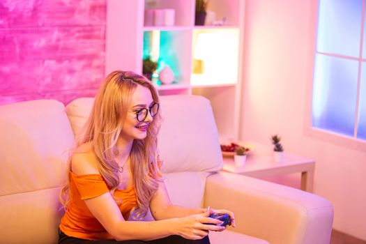 Beautiful blonde girl excited while playing video games using wireless controllers. Cheerful girl playing video games.